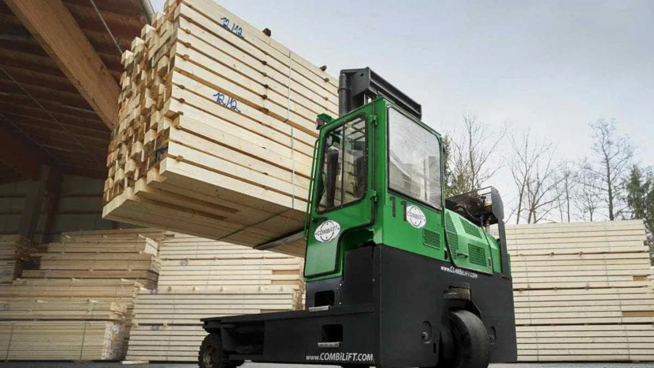A green Combilift multidirectional sideloader carrying a load of long timber lengths in a timber storage yard, with Combilift branding