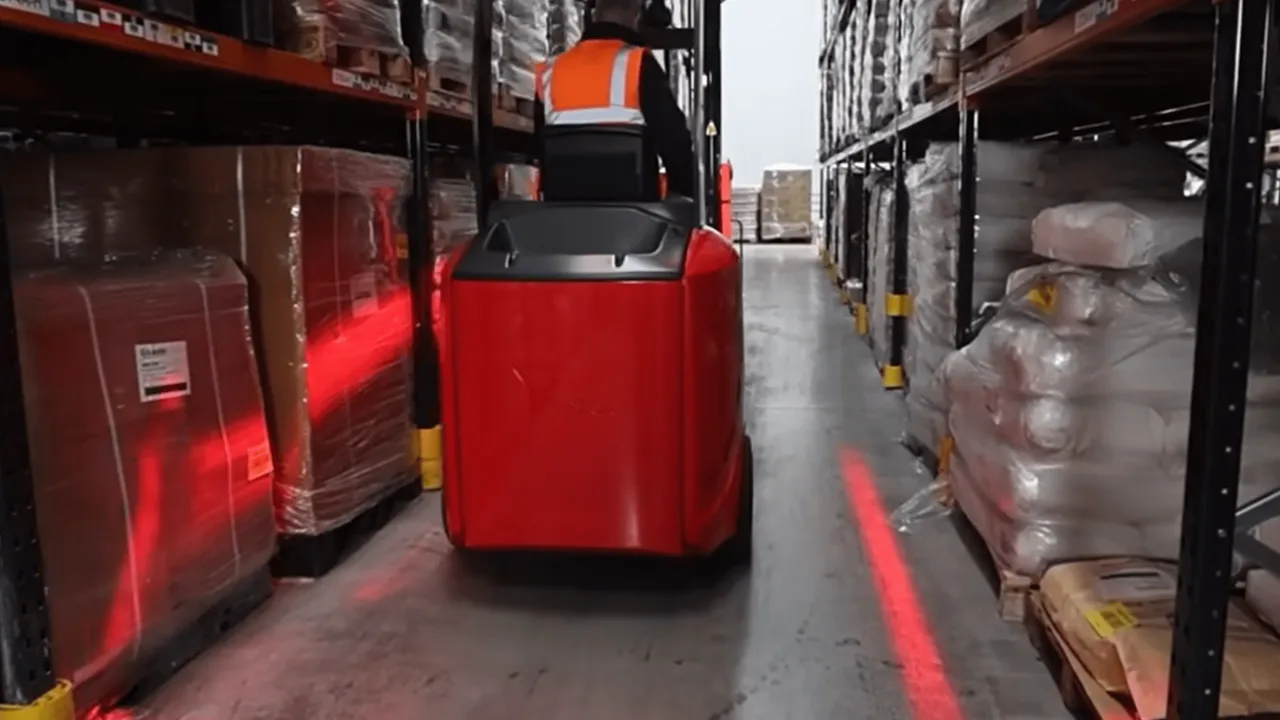 Articulated very narrow aisle forklift truck working between tall warehouse racking with a pallet raised high