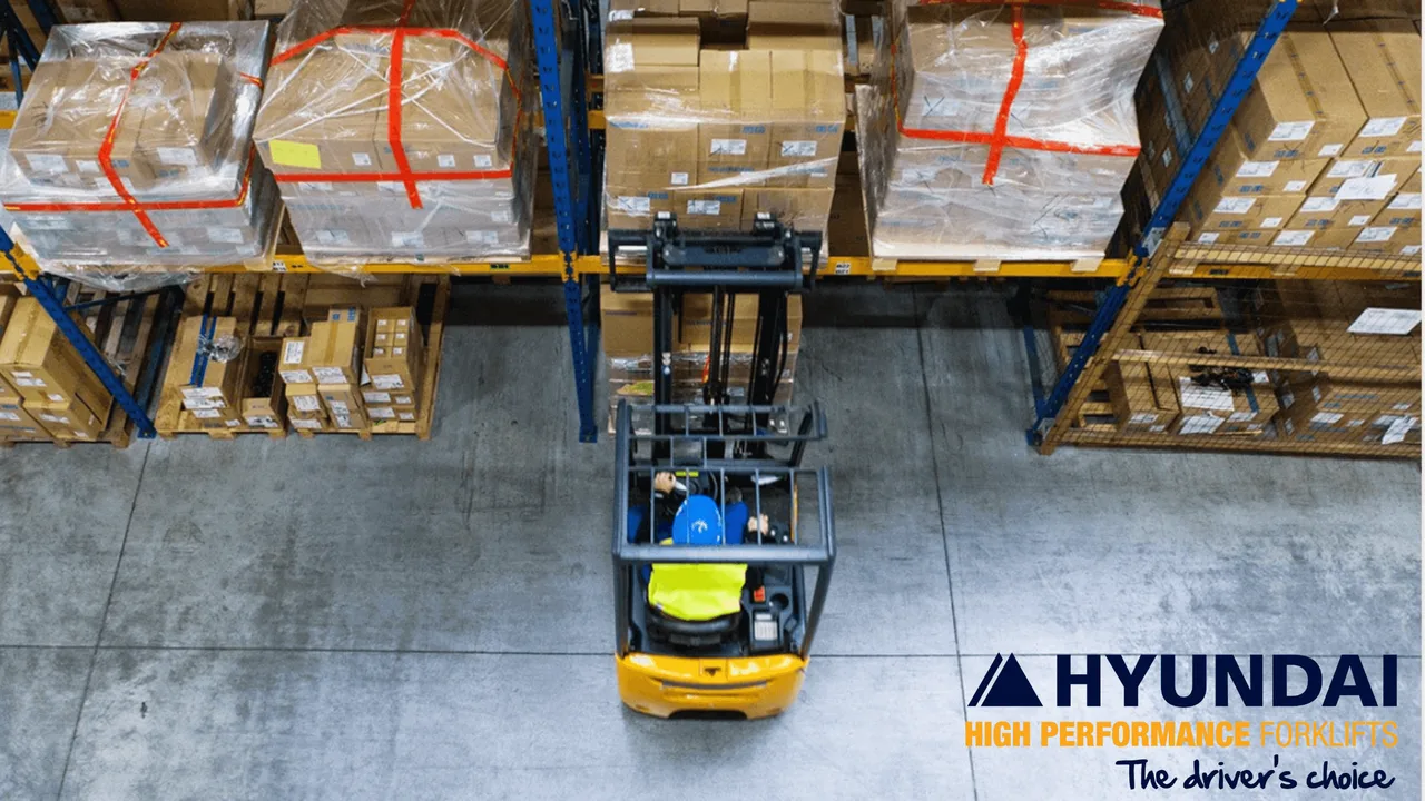 Overhead view of a Hyundai forklift truck working in a warehouse aisle beside a worker in hi vis, with Hyundai branding
