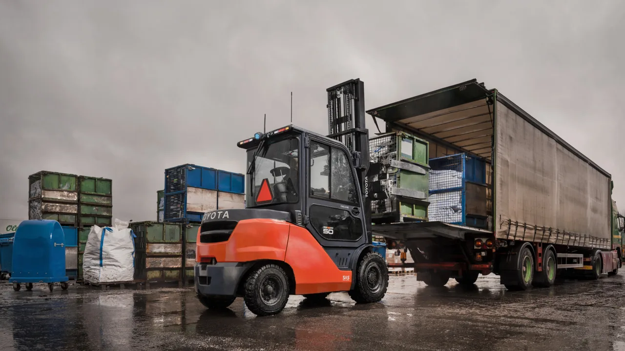 An orange Toyota counterbalance forklift truck loading a lorry trailer in a yard, with Toyota branding on the side